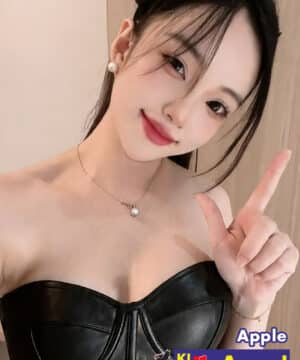 Portrait of a young woman in a black strapless top, making a peace sign, with jewelry and soft makeup; appears to be an escort ad badge in corner reading 'KL escort Angel' and contact number.